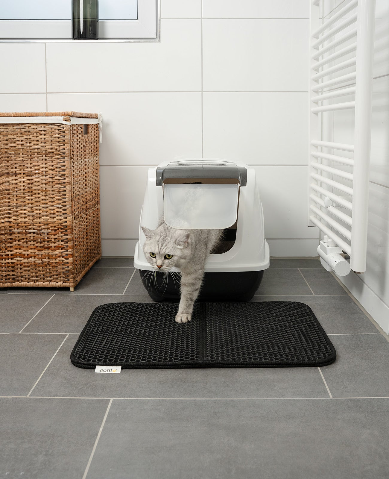 graue Katze steigt aus Katzentoilette im Badezimmer auf schwarze doppellagige Katzenstreumatte